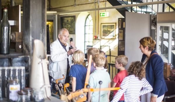 Kinderen en vrouw krijgen uitleg van een oud-mijnwerker in het Limburgs Mijnmuseum